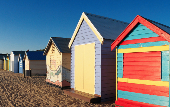 Different coloured beach huts in a row, disappearing into the distance
