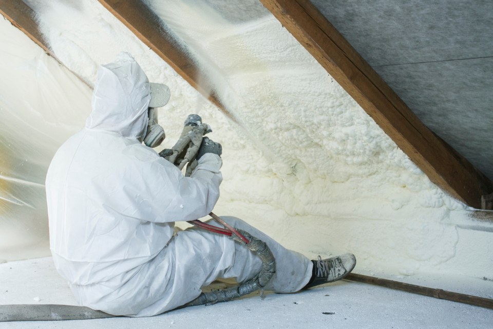 A person installing spray foam insulation between the roof joists in someone's loft