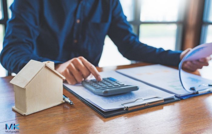A man in a suit sitting at a desk with a calculator, helping someone with a mortgage in principle