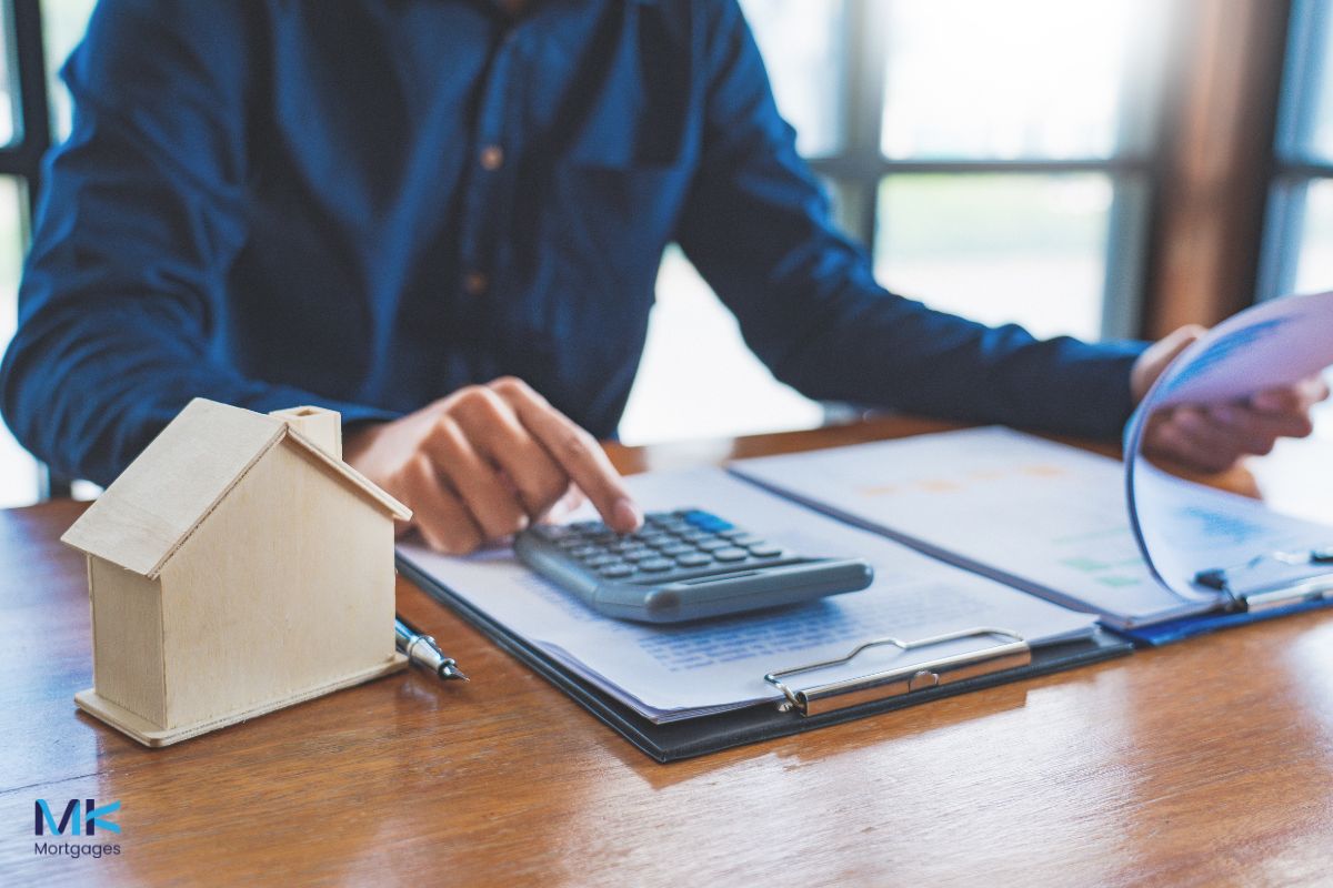 A man in a suit sitting at a desk with a calculator, helping someone with a mortgage in principle
