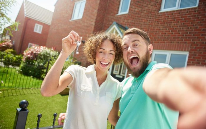 A couple outside their house with the keys. They are smiling because they are successful first time buyers.