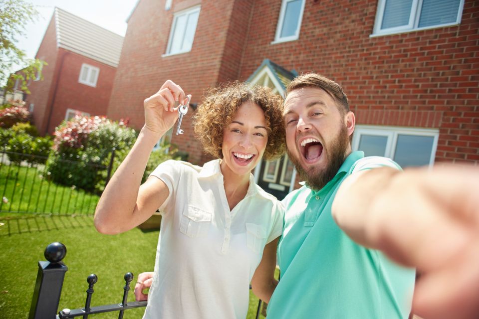 2025-09-09 Case Study – First Time Buyers June 2025 – header A couple outside their house with the keys. They are smiling because they are successful first time buyers.